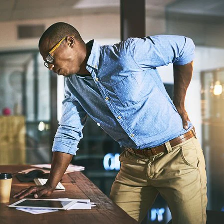 A Man With Back Pain is pictured, holding his lower back